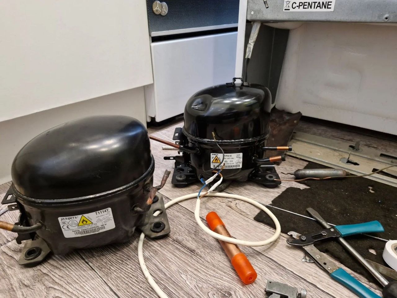 Дверца холодильника с логотипом Hotpoint Ariston и шильдиком модели; открытая нижняя панель и область с компрессором во время ремонта, ракурс 4