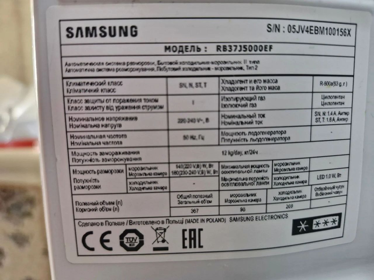 Открытая сервисная панель холодильника Samsung с видимыми электронными платами; снятая плата в руке мастера, ракурс 3